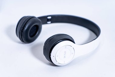 Siyah kulaklıklı şık kulaklıklar ve beyaz bir saç bandı, müzik dinlemeye ya da çağrılara cevap vermeye hazır, sade beyaz bir arkaplanda sergilenmektedir.