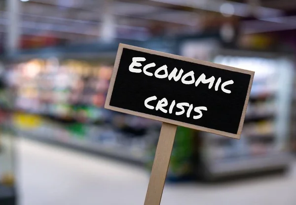 Houten Informatiebord Met Tekst Economische Crisis Tegen Onscherpe Winkelschappen Boodschap — Stockfoto