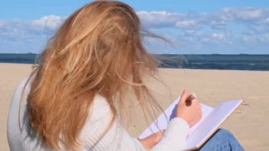 Deniz manzarasının yanındaki plajda not defteriyle ders çalışan genç bir öğrenci. Kahve içip kruvasan yemek. Minnettarlık günlüğü yazarken, kendini keşfetme, açık havada, sonbahar sıcağında.. 