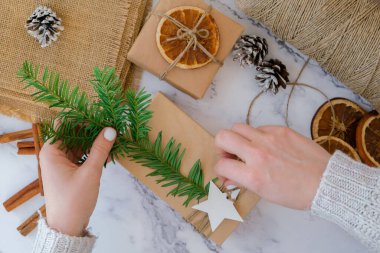 Yeni yıl hediyeleriyle kutu hazırlayan kadın, el işi kağıdına sarılmış ve köknar dallarıyla süslenmiş. Tatiller ve Hediyeler konsepti. El yapımı çevre dostu alternatif yeşil Noel sunar sıfır atık sürdürülebilir yaşam tarzı Top view yatıyordu