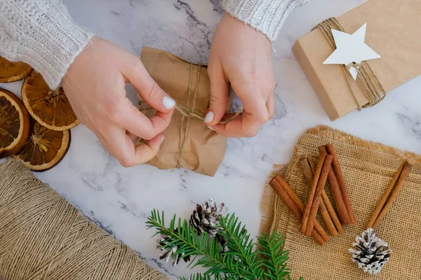 Woman making Box with New Year\'s gifts, wrapped in craft paper and decorated with cinnamon sticks. Holidays and Gifts concept. Handmade Eco friendly alternative green Christmas presents zero waste Sustainable lifestyle Top view