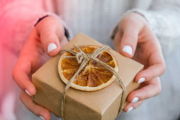 Woman giving Box with New Year\'s gifts, wrapped in craft paper and decorated with dry orange slices. Holidays and Gifts concept. Handmade Eco friendly alternative green Christmas presents zero waste Sustainable lifestyle