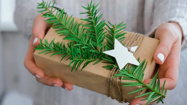 Woman giving Box with New Year\'s gifts, wrapped in craft paper and decorated with fir branch. Holidays and Gifts concept. Handmade Eco friendly alternative green Christmas presents zero waste Sustainable lifestyle