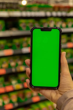 Mobile phone Chroma key. Close up of woman hand holds smart phone with green screen at shopping mall store. Buying food at supermarket, grocery shop center online. Department store. Gadgets