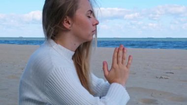 Genç bir kadın deniz kıyısında meditasyon yapıyor. Nefes almak zihinsel sağlığa iyi gelir. Nefes terapisi. Kundalini enerjisini her gün dengelemek kadın sağlığına iyi gelir.