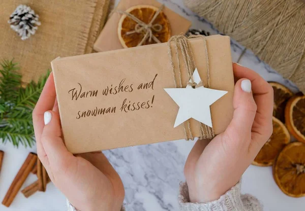 Warm wishes and snowman kisses Inspiration joke quote phrase Woman making Box with New Years gifts, wrapped in craft paper and decorated with fir branch. Holidays and Gifts concept. Handmade Eco