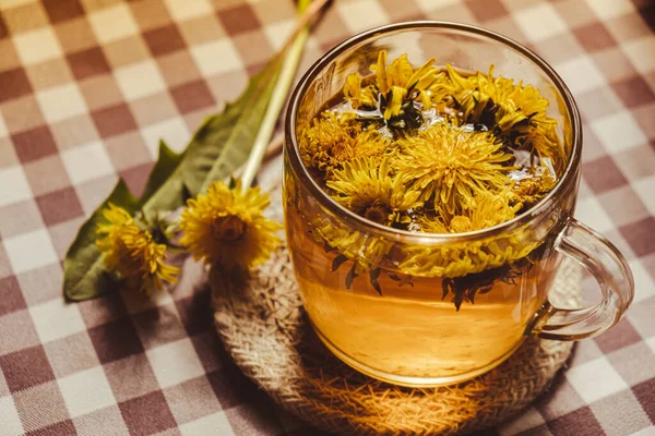 Dandelion flower healthy tea in glass cup on table. Herbal medicine Delicious tisane tea from with fresh yellow blossom dandelion flowers inside tea cup. Green clearing infusion Wildflowers Eco