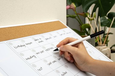Aylık Planlama 'da, randevuları ve gelecek ayın planlarıyla dolu bir kadın el yazısı. Yoğun bir ay programı var. Ayın günleriyle birlikte manyetik pano. Önemli konulara girilecek yer