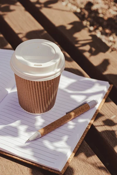 生态回收纸杯与咖啡或茶在牛皮纸与空白纸笔记本在木制长椅上 室外学习的概念 把咖啡拿走去 复制文本的空间 可处置硬纸板 — 图库照片