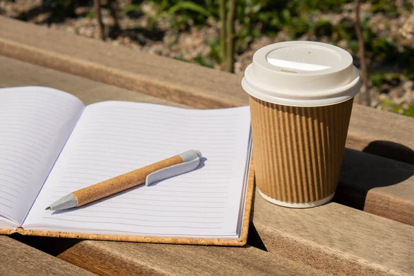 クラフト紙にコーヒーや紅茶を入れたエコリサイクル紙コップで 木製のベンチには空の紙ノートブックがあります 勉強の概念は屋外で働く コーヒーを飲みに行きなさい テキストのスペースをコピーします 使い捨ての段ボール — ストック写真