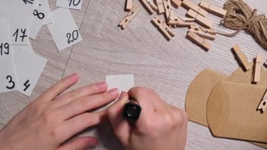Tanınmayan genç bir kadın el işi çantasına numara yapıştırıyor, mandalla tutturuyor. Ev yapımı takvim için el yapımı kraft kâğıdı yapan bir kadın. Kendi ellerinle adım adım kendin yap.
