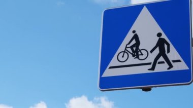Bisikletçi ve yaya yolu paylaşım tabelası. Yol tabelası yayalar ve bisikletler mavi gökyüzünün arka planında karşıdan karşıya geçebilirler.