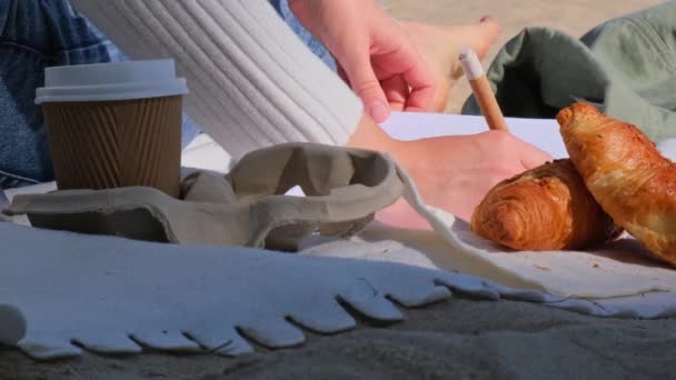 年轻的学生带着笔记本在海滩上学习 旁边是海洋景观 喝咖啡 吃羊角面包 写感恩日记自我反省自我发现户外温暖的秋天海滨 — 图库视频影像