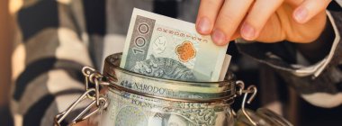 Polish zloty banknote saving money in glass jar. Unrecognizable woman moderate consumption and economy Collecting money. Tips. Business, finance, saving, banking and people concept. Extra money