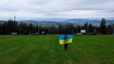 Ukrayna ulusal bayrağına sahip bir kadın, Gubalowka sıradağlarından alınan Tatra Dağları 'nın altındaki Zakopane kasabasının Vatanseverlik Havacılık görüşünü sallıyor. Drone High dağları ve yeşil tepeler yazın veya