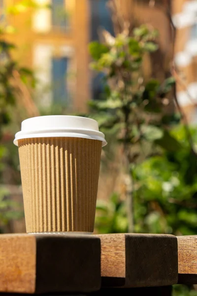 Eco recycling paper cup with coffee or tea on kraft paper on wooden table. Breakfast on the street in the park on bench. Take away coffee to go. Copy space for text. Disposable Cardboard coffee outdoors