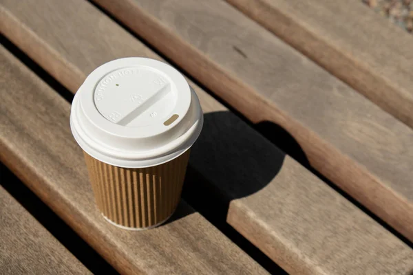 Eco recycling paper cup with coffee or tea on kraft paper on wooden table. Breakfast on the street in the park on bench. Take away coffee to go. Copy space for text. Disposable Cardboard coffee