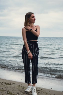 Young woman standing on blurred beachside background. Attractive female enjoying walking the sea shore. travel and active lifestyle concept. Springtime. Relaxation, youth, love, lifestyle solitude