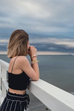 Young woman standing on wooden pier blurred beachside background. Attractive female enjoying the sea shore travel and active lifestyle concept. Springtime. Wellness wellbeing mental health inner peace