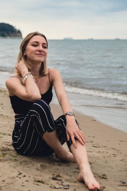 Young woman siting on blurred beachside background. Attractive female enjoying the sea shore. travel and active lifestyle concept. Springtime. Relaxation, youth, love, lifestyle solitude with nature