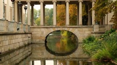 Baths classicist Palace on the Isle in Lazienki Park touristic place in Warsaw. Lazienki Royal Baths Park, Warsaw Poland. Colorful Autumn Foliage and Mirror Reflection on the Lake. Yellow leaves