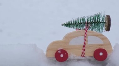 Wooden car carrying christmas tree over snow. Toy car in snowy landscape. Merry Christmas and Happy New Year concept. Winter is coming
