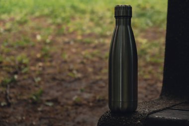 Water bottle. Reusable steel thermo water bottle on wooden bench. Sustainable lifestyle. Plastic free zero waste free living. Go green Environment protection. Health-conscious. Steel thermo water bottle of silver, on background of blurred grass. 