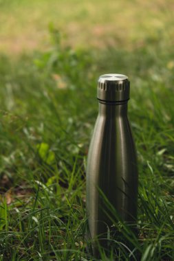 Water bottle. Reusable steel thermo water bottle on green grass. Sustainable lifestyle. Plastic free zero waste free living. Go green Environment protection. Health-conscious. Steel thermo water bottle of silver on background of blurred grass. 
