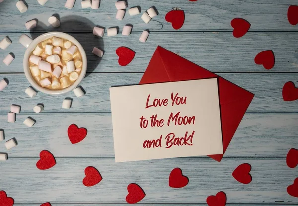 LOVE YOU TO THE MOON AND BACK text on valentine card inscription positive quote, motivation and inspiration phrase Greeting card with red envelope with white cup of coffee and marshmallows on wooden background. Romantic Small hearts Valentine day. Ho