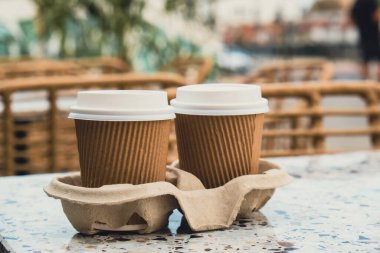Çay için kapaklı iki kağıt bardak. Masadan kahve al. Kahverengi kağıt bardak tutacağı olan kahve. Kahverengi güvenlik kartonundan tasmalar. Bardaklar için paket götür. Karton tepsi