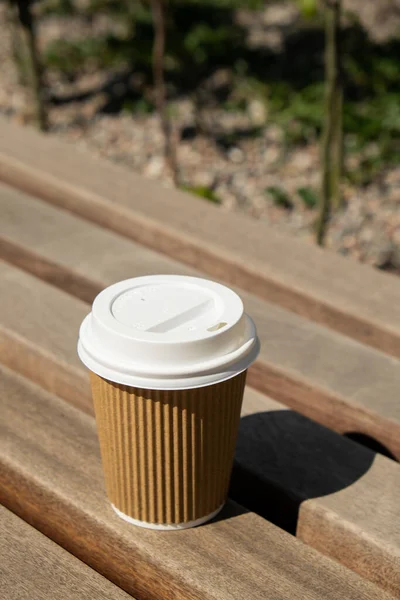 Eco recycling paper cup with coffee or tea on kraft paper on wooden table. Breakfast on the street in the park on bench. Take away coffee to go. Copy space for text. Disposable Cardboard coffee outdoors