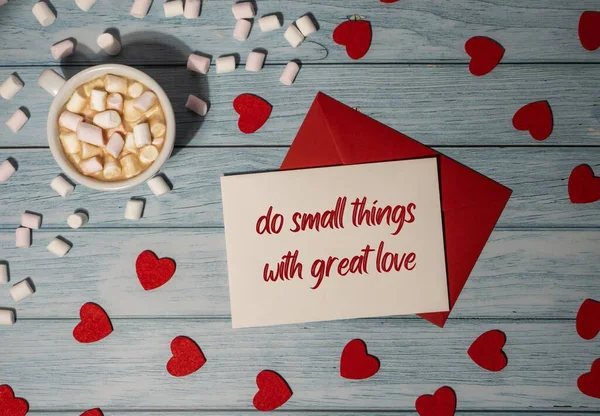 DO SMALL THINGS WITH GREAT LOVE text inscription positive quote, motivation and inspiration phrase. Greeting card with red envelope with white cup of coffee and marshmallows on wooden background. Romantic Small hearts Valentine day. Holiday morning.