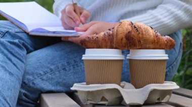 Park yerinde not defteriyle ders çalışan genç bir öğrenci. Kahve içip kruvasan yemek. Minnettarlık günlüğü yazarken, kendini keşfetme, açık havada, sonbahar sıcağında.. 