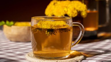 Dandelion flower healthy tea in glass teapot and glass cup on table. Delicious herbal tea from fresh dandelion flowers at home at summer day. Green clearing Hot dandelion tea in a glass teapot