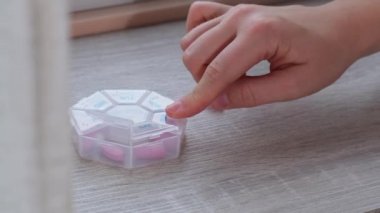 Hapları düzenleyen kadın eller haftalık tıbbi hap kutularını günlük haplarla kapatıyorlar. İlaçları beyaz pembe haplar ve kapsüllerle alıyorlar. Genç bir kadın günlük vitaminlerini alıyor.