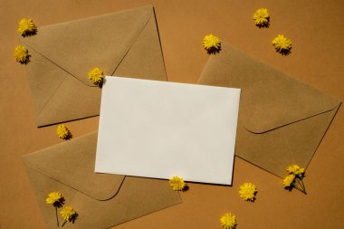 Beautiful little yellow chamomile daisies flowers on postal yellow envelopes on beige background, empty paper note copy space for text, spring time, greeting card for holiday. Flower delivery. Delicate yellow flowers