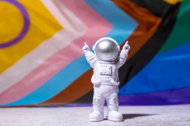 Toy astronaut on Rainbow LGBTQIA flag made from silk material background. Happy pride month. Symbol of LGBTQ pride month. Equal rights. Peace and freedom. Support LGBTQIA community. Diversity equality