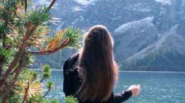 Young woman enjoying Tatra National Park, Poland. Tourist in Famous Mountains Lake Morskie Oko Or Sea Eye Lake In autumn. Snow covered mountain peaks on background. Blue water nature landscape 4k