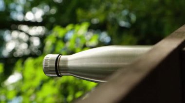 Su şişesi. Ahşap bank izometrik konseptinde yeniden kullanılabilir çelik termo su şişesi. Sürdürülebilir yaşam tarzı. Plastiksiz sıfır atıksız yaşam. Yeşil çevre korumasına geçin. Sağlık bilinci yerinde. Çelik