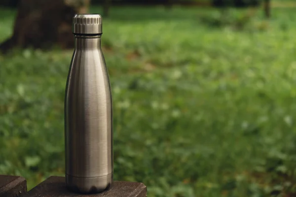 Water bottle. Reusable steel thermo water bottle on green grass. Sustainable lifestyle. Plastic free zero waste free living. Go green Environment protection. Health-conscious. Steel thermo water bottle of silver, on background of blurred grass.
