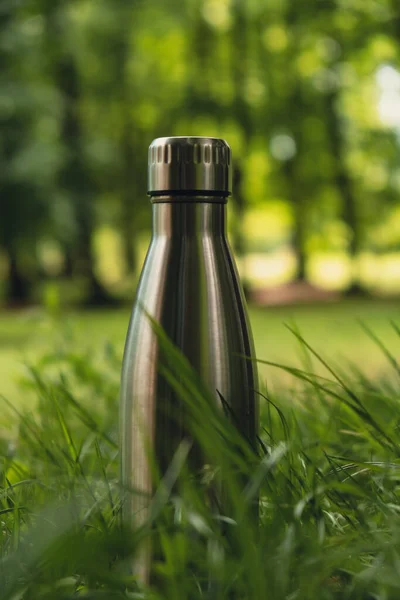 Water bottle. Reusable steel thermo water bottle on green grass. Sustainable lifestyle. Plastic free zero waste free living. Go green Environment protection. Health-conscious. Steel thermo water bottle of silver on background of blurred grass.