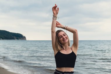 Young woman standing on blurred beachside background. Attractive female enjoying walking the sea shore. travel and active lifestyle concept. Springtime. Relaxation, youth, love, lifestyle solitude with nature. Wellness wellbeing mental health inner p