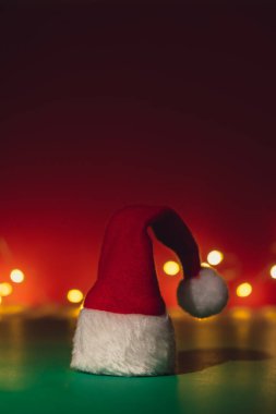 Santa hat on isometric green red background. Defocused lights on backdrop Copy space for your text. Mock up for advertisement. Holiday Christmas composition. Minimalistic greeting card. Creative 