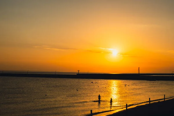Silhouette of people enjoying sea and summer days. Reflection of sunlight over sea surface at sunset. Orange and gold blue sky. Scenic Gold sea. Dramatic Yellow sun coming out of the sea. Majestic summer landscape