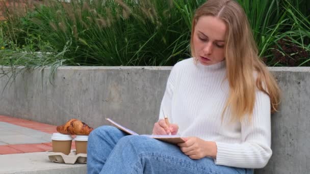 公園のノート付きの若い学生の勉強 コーヒーを飲み クロワッサンを食べる 感謝日記自己反省自己発見を書く屋外暖かい秋の海岸 — ストック動画