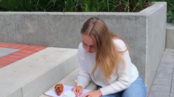 Молодий Студент Навчається Блокнотом Парку Пити Каву Їсти Круасани Написання — стокове відео