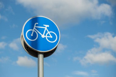 Round road sign depicting white bicycle on blue background, meaning mandatory bike path for cyclists against blue sky background. Blue round sign on bike path pole. Bike path