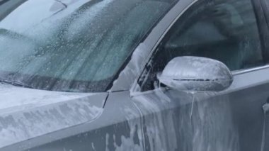 Washing luxury silver car on touchless car wash. Washing sedan car with foam self-service and high pressure water. Winter cleaning in car wash. Cleanliness and order in urban environment