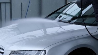 Washing luxury silver car on touchless car wash. Washing sedan car with foam self-service and high pressure water. Winter cleaning in car wash. Cleanliness and order in urban environment