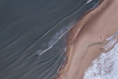 Winter in cold Baltic sea snowy beach in Gdansk. Aerial view of snow covered beach and dunes and dark calm sea nature landscape captured with drone. Winter tourism in Poland